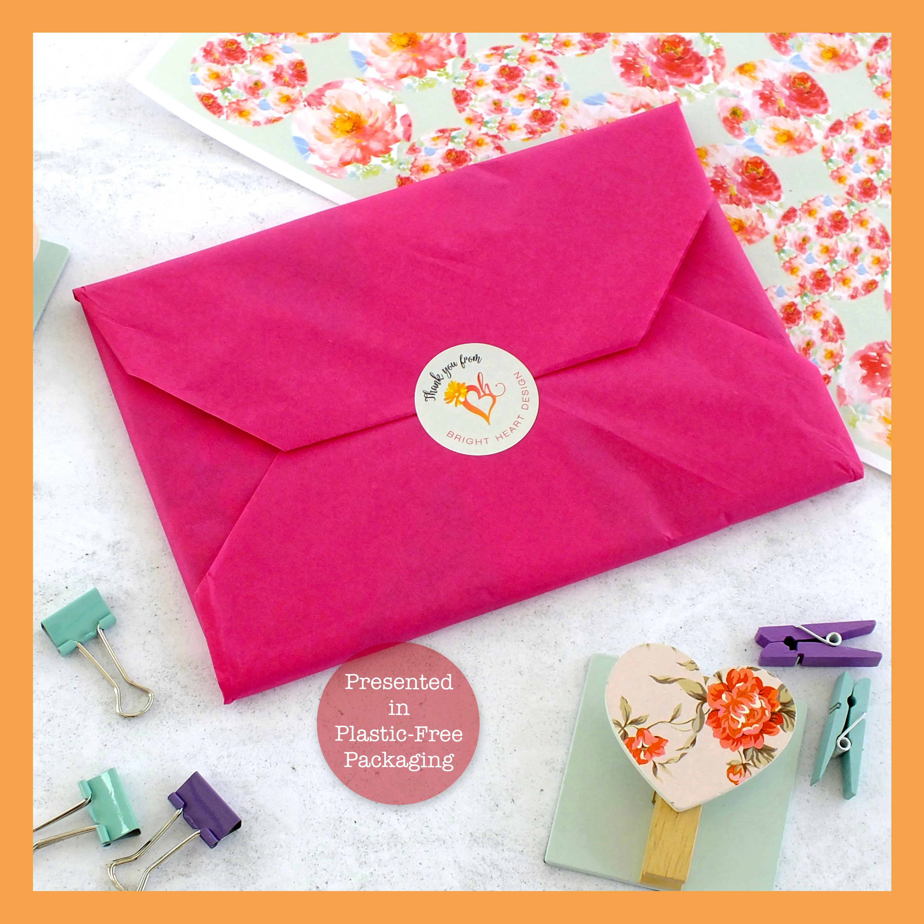 Pink envelope with a floral design on a white surface with office supplies.